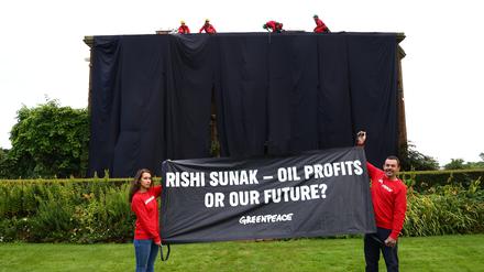 Greenpeace-Aktivisten haben ein Haus verhüllt und halten ein Plakat mit der Aufschrift „Rishi Sunak –  Ölprofite oder unsere Zukunft?“