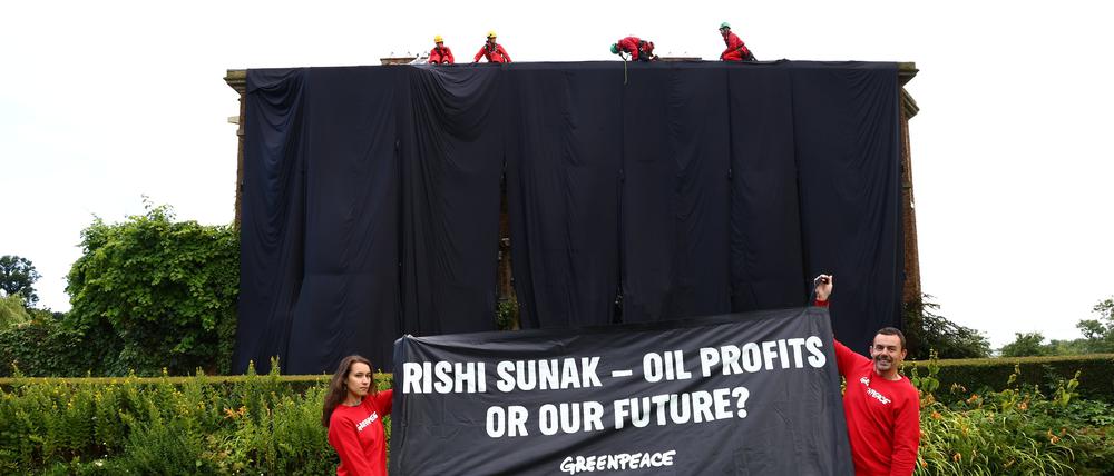 Greenpeace-Aktivisten haben ein Haus verhüllt und halten ein Plakat mit der Aufschrift „Rishi Sunak – Ölprofite oder unsere Zukunft?“