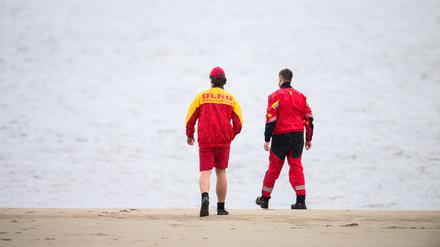Zwei Mitarbeiter der DLRG gehen an der Elbe entlang.