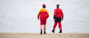 Zwei Mitarbeiter der DLRG gehen an der Elbe entlang.