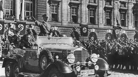 In einem Auto stehend grüßt Adolf Hitler die ihm zujubelnde Menschenmenge in Wien.