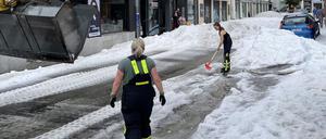 Einsatzkräfte der Feuerwehr räumen Hagel von einer Straße. 