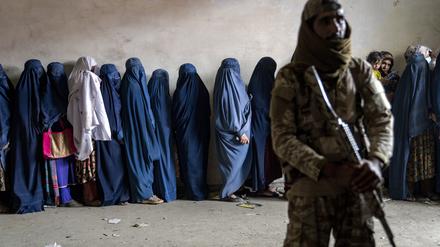 Ein Taliban-Kämpfer steht Wache, während afghanische Frauen darauf warten, von einer humanitären Hilfsorganisation verteilte Lebensmittelrationen zu erhalten.