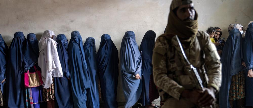 Ein Taliban-Kämpfer steht Wache, während Frauen darauf warten, von einer humanitären Hilfsorganisation verteilte Lebensmittelrationen zu erhalten.
