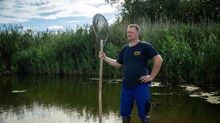 PRODUKTION - 05.08.2023, Brandenburg, Kuhbrücke: Fischer Andre Schneider steht in der Oder. Die Familie Schneider betreibt einen Fischereihof mit Campingplatz und Imbiss an der Oder. Unzählige tote Fische verwesten im Sommer 2022 in der Oder. Auch Deutschlands einziger Auen-Nationalpark an der Oder war in Gefahr. Schneider hofft, dass das «Thema Oder» nicht im Politikalltag untergeht. «Der Fluss ist für uns Existenz, Lebensader, Hoffnung», sagt der an der Oder Aufgewachsene. (zu dpa "Ein Jahr nach dem Fischsterben - Bislang noch mal Glück gehabt?") Foto: Hannes P. Albert/dpa +++ dpa-Bildfunk +++