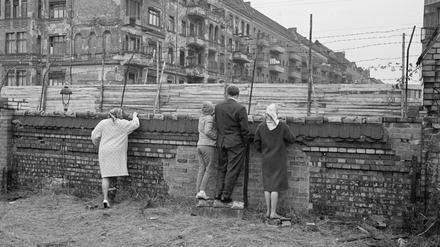 Menschen blicken über Mauer und Stacheldraht auf den „Todesstreifen“. 