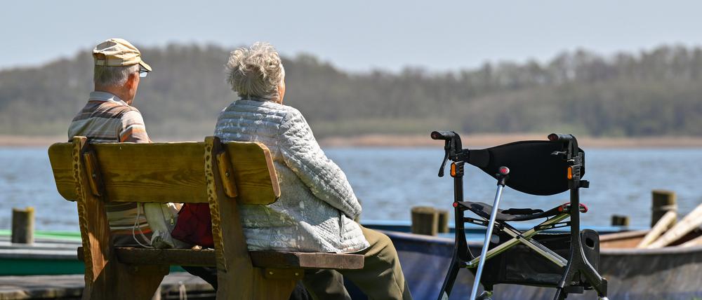 Ein älteres Paar sitzt auf einer Bank am Ufer eines Sees und genießt das sonnige Frühlingswetter.