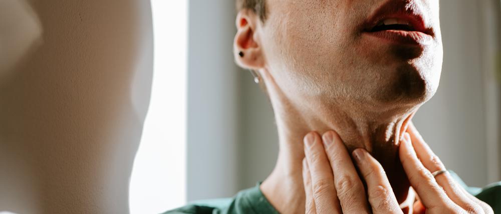 An unrecognisable man touches his neck / throat as if in pain. Conceptual with space for copy.