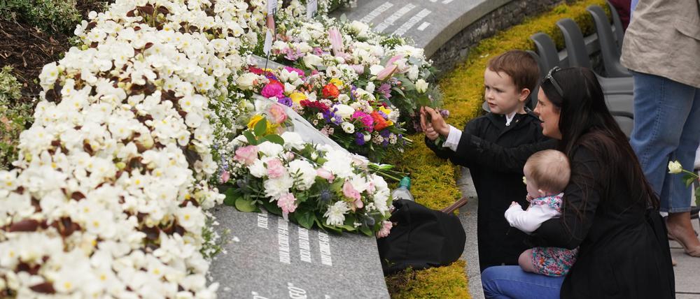 Eine Frau legt im Memorial Garden mit ihren zwei Kindern Blumen nieder während eines Gottesdienstes zum 25. Jahrestag eines Attentats. Die Explosion einer Autobombe in der nordirischen Stadt Omagh am 15. August 1998 jährt sich zum 25. Mal.