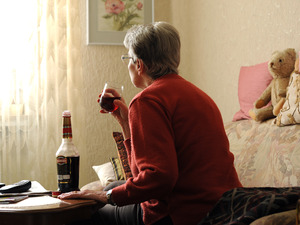 Eine Frau sitzt in einer Wohnung und trinkt Alkohol.