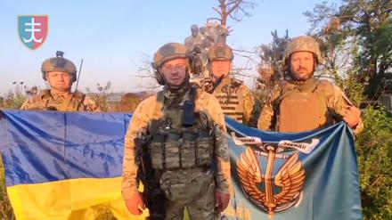 Ukrainische Soldaten stehen mit der ukrainischen Flagge in Uroschajne.