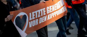 Demonstranten laufen auf einer Demoder Klimagruppe Letzte Generation mit einem Banner mit der Aufschrift ·letzte Generation vor den Kipppunkten· über den Potsdamer Platz.