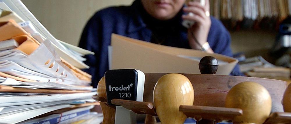 Eine Mitarbeiterin des Landratsamts sitzt telefonierend hinter zahlreichen Akten und Stempeln an ihrem Arbeitsplatz.