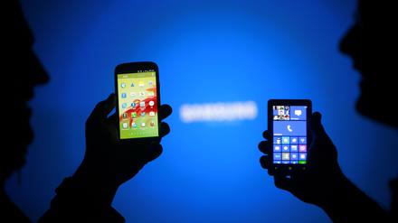 Men are silhouetted against a video screen as they pose with Samsung Galaxy S3 and Nokia Lumia 820 smartphones in this photo illustration taken in the central Bosnian town of Zenica, May 17, 2013. REUTERS/Dado Ruvic (BOSNIA AND HERZEGOVINA - Tags: BUSINESS TELECOMS)