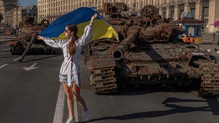 Eine Frau posiert mit ukrainischer Flagge vor einem zerstörten russischen Panzer.