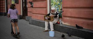 Alltagsszenen aus Charkiw: Ein Mädchen fährt auf einem Roller die Straße herunter, ein Mann füttert Tauben.