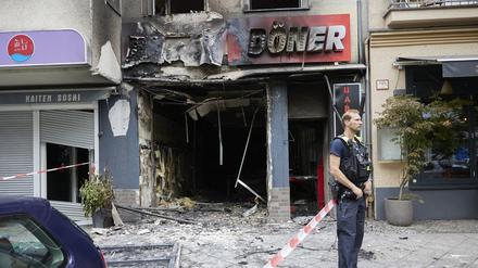Ein Polizist steht vor einem ausgebrannten Dönerimbiss in der Uhlandstraße. Das Brandkommissariat ermittelt nun dem Polizeisprecher zufolge in alle Richtungen. Zwei Menschen mit über den Kopf gezogenen Kapuzen sollen sich vom Brandort entfernt haben.