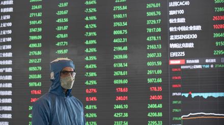 03.02.2020, China, Shanghai: Ein Arbeiter in einem Schutzanzug steht vor einer elektronischen Anzeigetafel in der Lobby des Börsengebäudes der Shanghai Stock Exchange. Chinas Wirtschaft erholt sich kaum von der Pandemie.