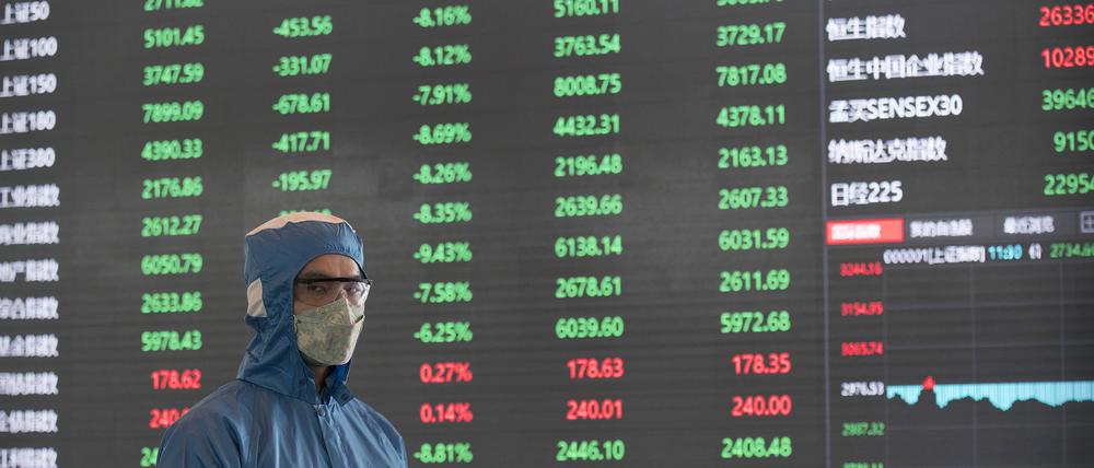 03.02.2020, China, Shanghai: Ein Arbeiter in einem Schutzanzug steht vor einer elektronischen Anzeigetafel in der Lobby des Börsengebäudes der Shanghai Stock Exchange. Chinas Wirtschaft erholt sich kaum von der Pandemie.