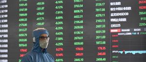 03.02.2020, China, Shanghai: Ein Arbeiter in einem Schutzanzug steht vor einer elektronischen Anzeigetafel in der Lobby des Börsengebäudes der Shanghai Stock Exchange. Chinas Wirtschaft erholt sich kaum von der Pandemie.