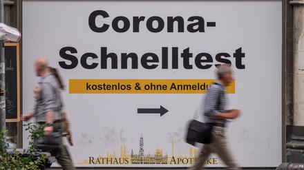 Passanten gehen in der Fußgängerzone in der Innenstadt an einem Plakat mit der Aufschrift ·Corona-Schnelltest - kostenlos und ohne Anmeldung· vorbei. (Symbolbild)