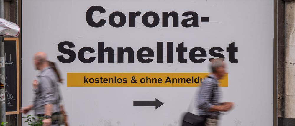 Passanten gehen in der Fußgängerzone in der Innenstadt an einem Plakat mit der Aufschrift ·Corona-Schnelltest - kostenlos und ohne Anmeldung· vorbei. (Symbolbild)