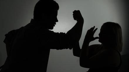 Ein als Silhouette abgebildeter Mann droht einer Frau mit der Faust.