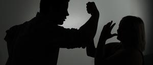 Ein als Silhouette abgebildeter Mann droht einer Frau mit der Faust.