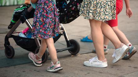 Eine Frau schiebt einen Kinderwagen und geht begleitet von mehreren Kindern.