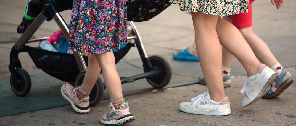 Eine Frau schiebt einen Kinderwagen und geht begleitet von mehreren Kindern.