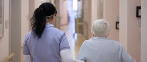 Eine Pflegefachkraft geht mit einer Pflegeheim-Bewohnerin über den Gang.