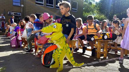 Kinder bei der Einschulung mit Ihren Schultüten auf dem Schulhof, im Vordergrund ein Kind mit Dinosaurier-Schultuete.
