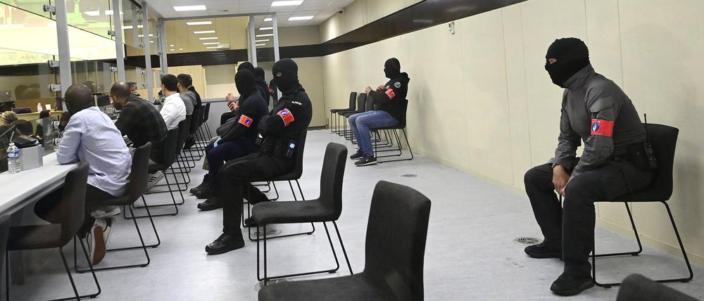 Glasbox im Gerichtssaal: bewacht von vermummten Polizisten.