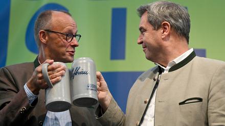 Beim politischen Frühschoppen Gillamoos. Friedrich Merz (l), Bundesvorsitzender der CDU, und Markus Söder (CSU), Ministerpräsident von Bayern, stoßen auf der Bühne mit Bierkrügen an. 