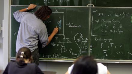 Ein Lehrer schreibt im Physik-Unterricht Formeln an die Tafel, Symbolbild.