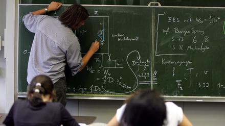 Ein Lehrer schreibt im Physik-Unterricht Formeln an die Tafel.