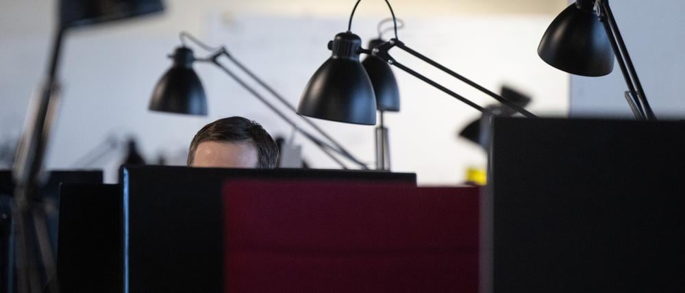 Ein Mann arbeitet am Computer in einem Büro mit zahlreichen Arbeitsplätzen (Symbolbild).