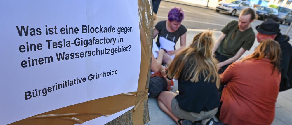 07.09.2023, Brandenburg, Fürstenwalde/Spree: Vor dem Amtsgericht von Fürstenwalde sitzen Klimaaktivisten auf dem Gehweg und daneben hängt ein Zettel mit der Aufschrift «Was ist eine Blockade gegen eine Tesla-Gigafactory in einem Wasserschutzgebiet? Bürgerinitiative Grünheide». Am selben Tag begann der Prozess am Amtsgericht Fürstenwalde gegen drei Klimaaktivisten, die wegen gefährlichen Eingriffs in den Straßenverkehr, bei einer Protestaktion beim US-Elektroautobauer Tesla, dabei waren. Foto: Patrick Pleul/dpa +++ dpa-Bildfunk +++