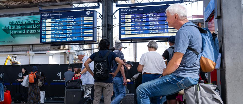 Reisende warten im Hauptbahnhof vor einer Anzeigetafel.