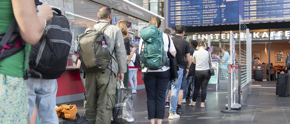 Reisende stehen im Berliner Hauptbahnhof am DB-Infoschalter.