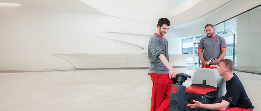 Ein Ausbilder erklärt zwei Azubis die Bedienung einer Bodenreinigungsmaschine.