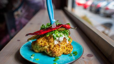 Gebackener Blumenkohlkopf, serviert mit Kurkuma-Aioli, Tahini, Koriander, Frühlingszwiebeln und Chilis.