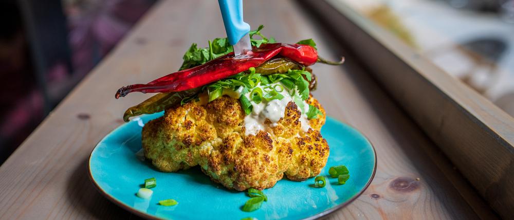 Gebackener Blumenkohlkopf, serviert mit Kurkuma-Aioli, Tahini, Koriander, Frühlingszwiebeln und Chilis.