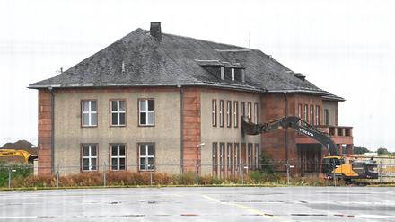 Ein Bagger steht mit umgedrehter Schaufel an dem zum Abriss vorgesehenen ehemaligen Generalshotel auf dem Gelände des Flughafens Berlin Brandenburg (BER).