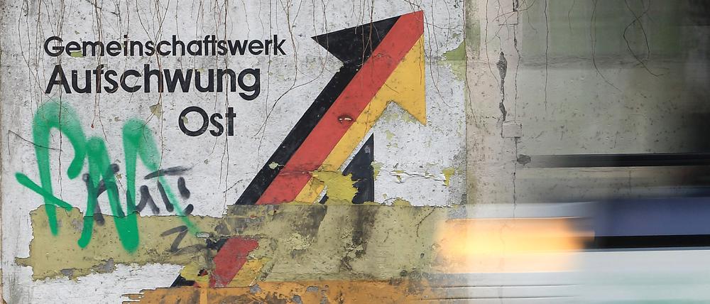 ARCHIV - 19.11.2013, Sachsen-Anhalt, Magdeburg: Am Schriftzug «Gemeinschaftswerk Aufschwung Ost» rollt eine Straßenbahn vorbei. Die Lebensverhältnisse gleichen sich 33 Jahre nach der Deutschen Einheit langsam weiter an, doch sind Löhne und Wirtschaftskraft in Ostdeutschland immer noch niedriger als im Westen. 
