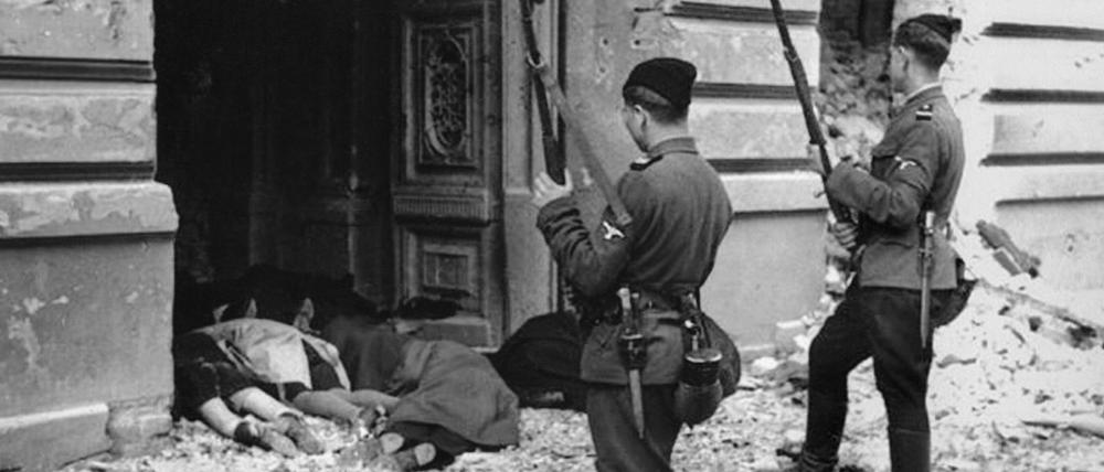 Niederschlagung des Aufstandes im Warschauer Ghetto (1943): Zwei Soldaten „fremdvölkischer Hilfseinheiten“ der SS stehen vor den Leichen getöteter Juden in einem Hauseingang.