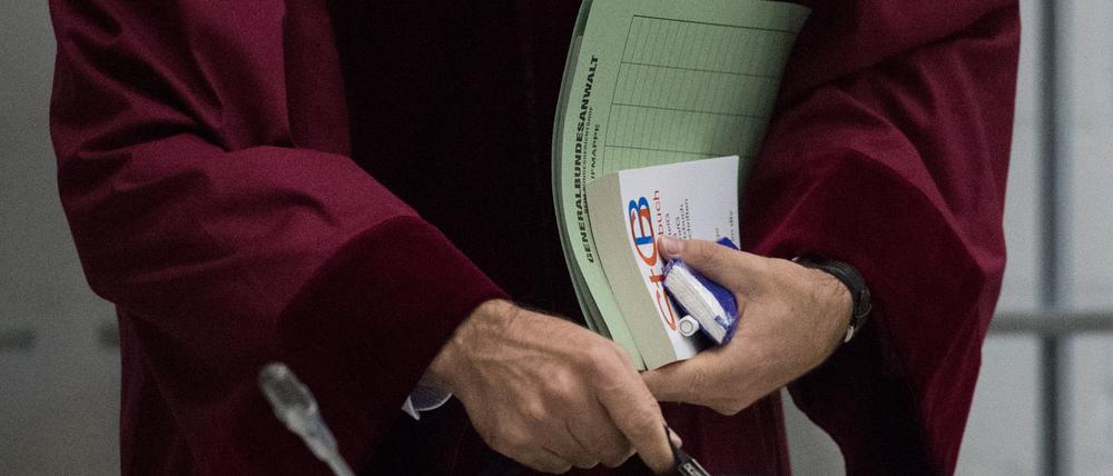 Ein Staatsanwalt beim Bundesgerichtshof hält am 14.09.2017 in Oberlandesgericht Stuttgart, Stuttgart-Stammheim (Baden-Württemberg) zu Beginn eines Prozesses eine Mappe und ein Strafgesetzbuch in der Hand.