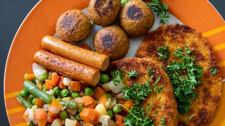 Vegane Falafel, vegane Schnitzel, vegane Würstchen und Gemüse sind auf einem Teller in einer Küche zu sehen.
