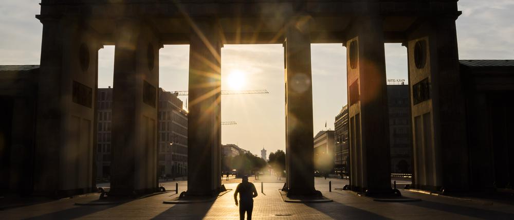 Ein Mann läuft bei aufgehender Sonne durch das Brandenburger Tor.