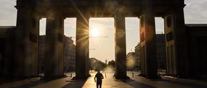 Ein Mann läuft bei aufgehender Sonne durch das Brandenburger Tor.